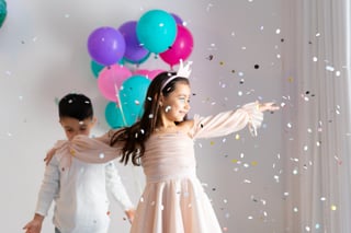 Girl in pink dress dancing joyfully with confetti and balloons
