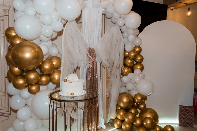 A beautifully styled first birthday party features a stunning white and gold balloon arch.