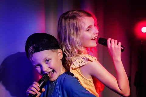 Happy boy and girl duet sing in microphones. karaoke party, children concert performance. neon lights