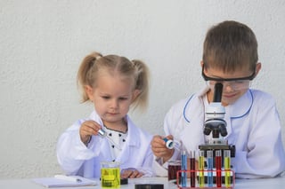 Cute children in lab coats playing with microscope and test tubes