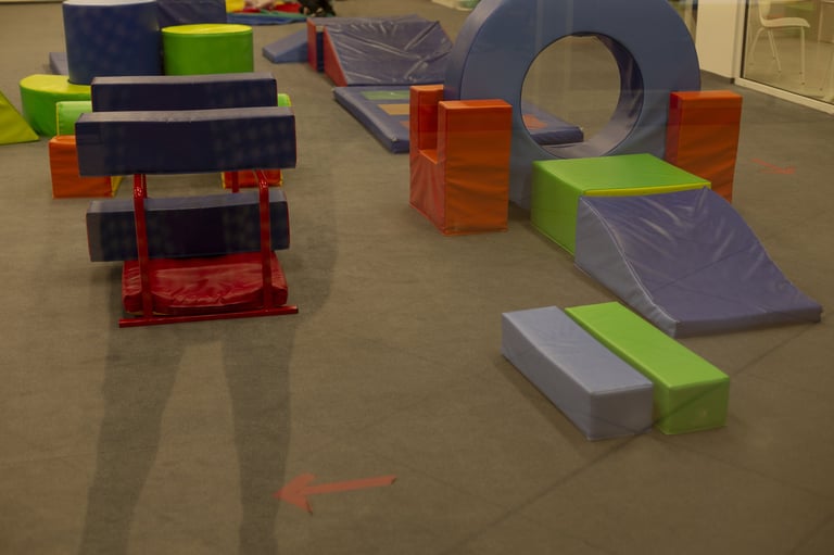 Soft foam circuit arranged for movement blue tunnel arch, angled platforms, low ramps, textured mats on beige carpet, geometric