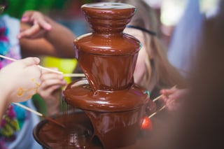 Vibrant Picture of Chocolate Fountain Fontain on childen kids birthday party with a kids playing around and marshmallows and fruits dip dipping into fountain