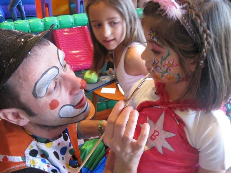 Two children holding a colorful inflatable clown toy with a smiling painted face at what appears to be an indoor play area