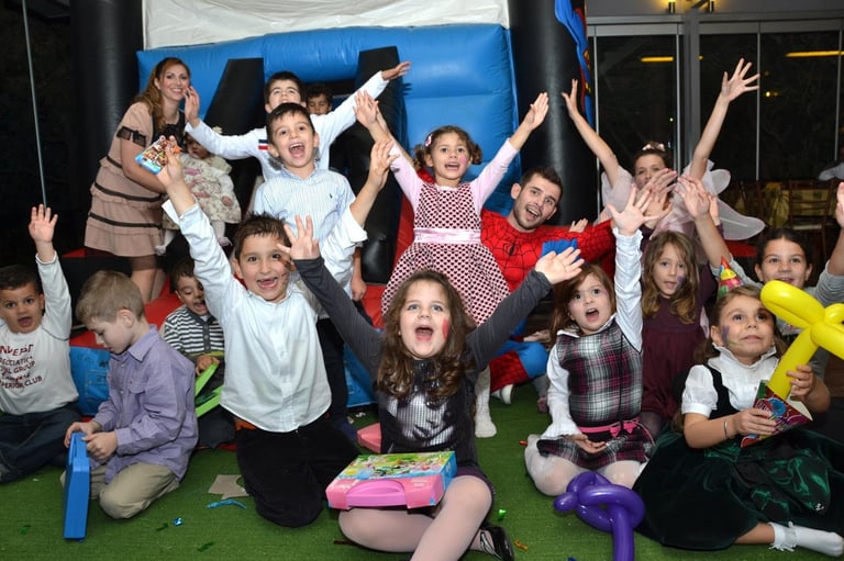 Group of children celebrating and posing with raised arms in front of a blue inflatable structure at an indoor party or event