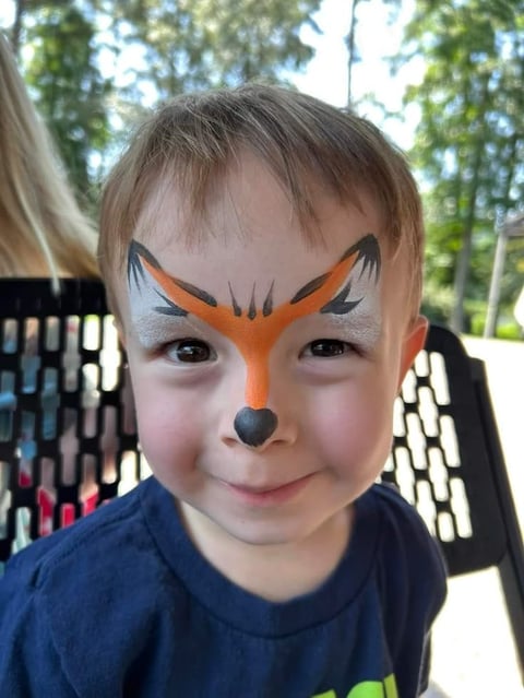 Young child with orange and black fox face paint outdoors in a park