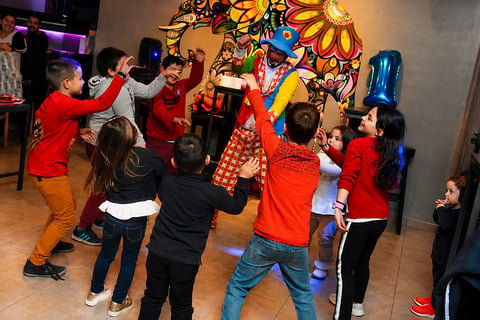 Group of children dancing and celebrating together in an indoor space with colorful artwork on the wall behind them