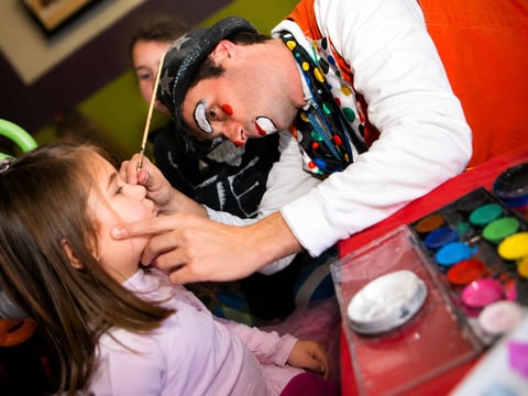 Face painter applies colorful makeup to a childs face during an indoor activity or event