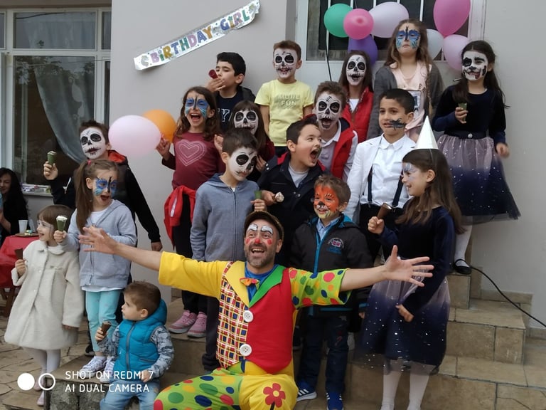 Large group of children and adults wearing Halloween and skeleton costumes at a birthday party with balloons and decorations