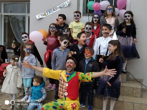 Group of children in Halloween costumes and face paint at a birthday party with colorful balloons and a birthday banner